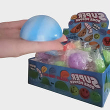 Hand reaching into a box of colorful 'Super Dome Popper' toys with packaging visible.