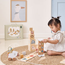 Child playing with wooden blocks and toys on a rug, with a framed picture of a duck in the background.