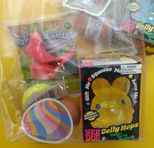 Assorted children's toys including a pink bird, green ball, and yellow bunny in packaging.