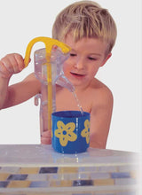 Child pouring water from a yellow and clear pitcher into a blue cup with yellow flowers on a white background