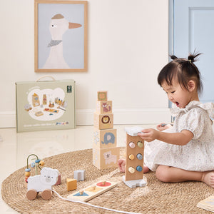 Child playing with wooden blocks and toys on a rug, with a framed picture of a duck in the background.