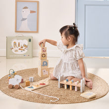 Child playing with wooden toys on a round mat in a room with a light blue wall and framed picture.