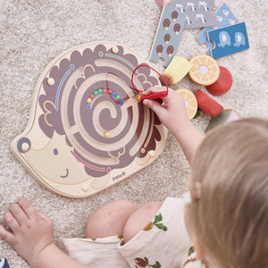 Child playing with a wooden hedgehog maze toy on a carpeted floor. fine motor toys