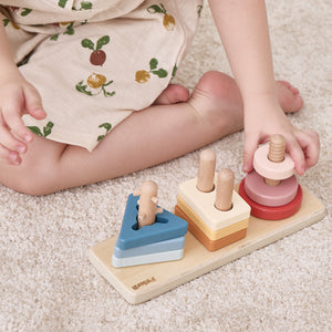 Child playing with a wooden shape sorting toy on a carpeted floor. wooden puzzle