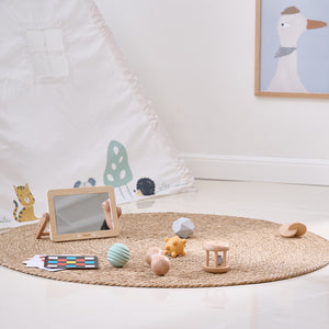 Children's toys on a woven mat in a room with a mirror and framed picture on the wall.