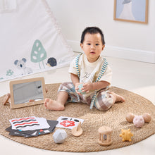 Baby sitting on a rug with toys and educational materials in a room.