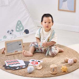Baby sitting on a rug with toys and educational materials in a room.