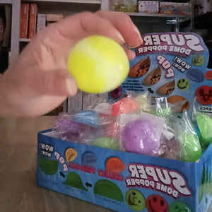 Hand holding a yellow Super Poper dome popper toy with packaging in the background.