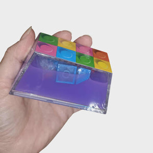 Hand holding a transparent cube with colorful block inserts on a white background Putty bricks