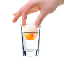 Hand placing a small ball into a clear glass on a white background