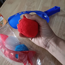 Hand holding a red water ball with blue handle on a wooden surface