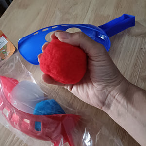 Hand holding a red water ball with blue handle on a wooden surface