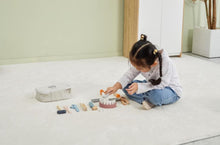 Child playing with toy kitchen set on a light-colored floor.