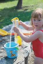 Child playing with water from a pump in a blue bucket outdoors.