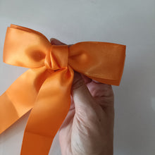 Orange ribbon bow held by a hand against a plain background
