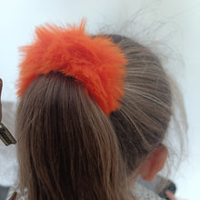 Person wearing an orange fluffy headband with a blurred background