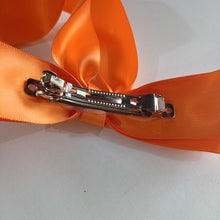 Metallic hair clip on an orange ribbon against a white background