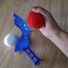 Hand holding a water red ball next to a blue toy bow and white ball on a wooden surface